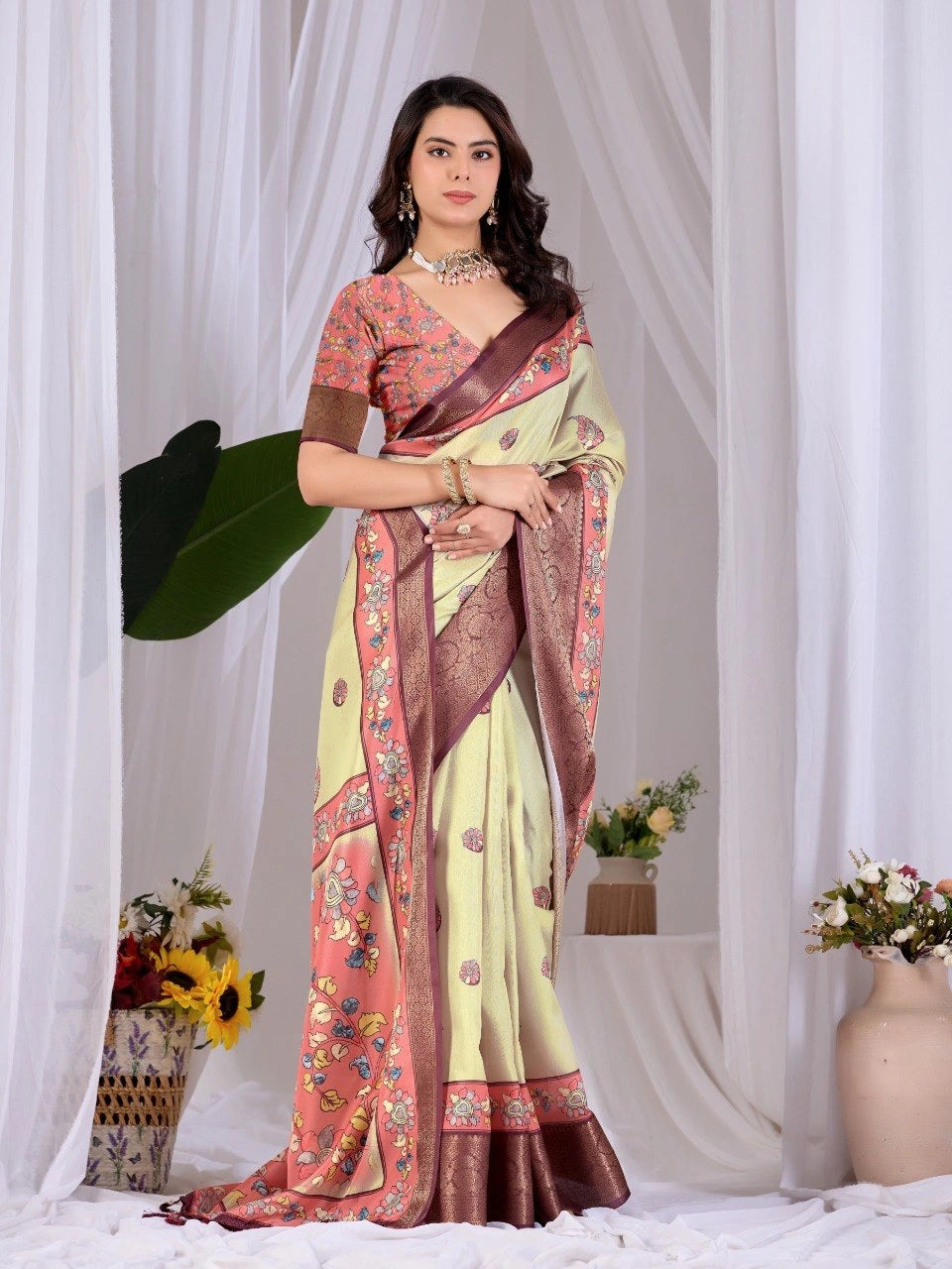 Woman wearing a traditional saree with a floral pattern against a white curtain background