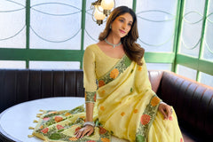 Woman in a yellow saree with floral patterns sitting on a couch.