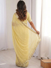 Woman wearing a yellow saree with gold border in a room with white curtains.