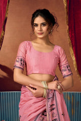 Woman wearing a pink saree with a traditional design against a brown and red background
