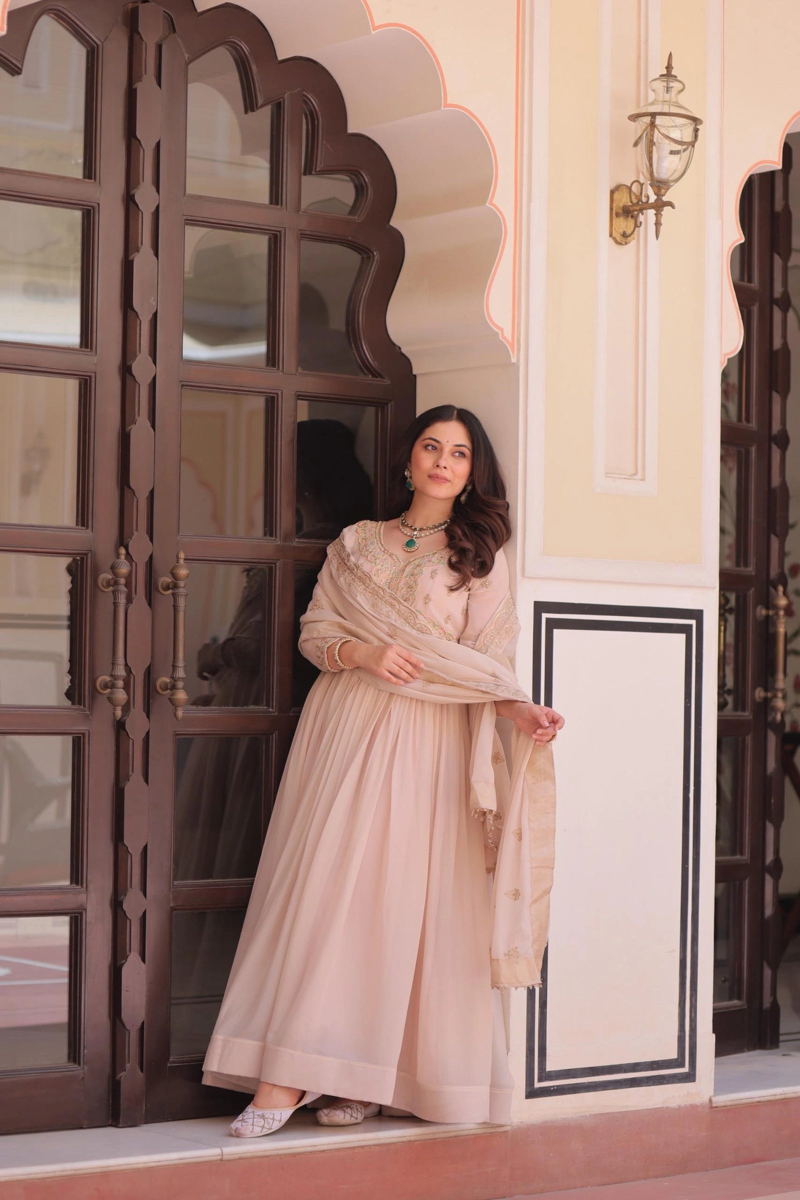 Woman in a beige dress standing in front of an ornate door.