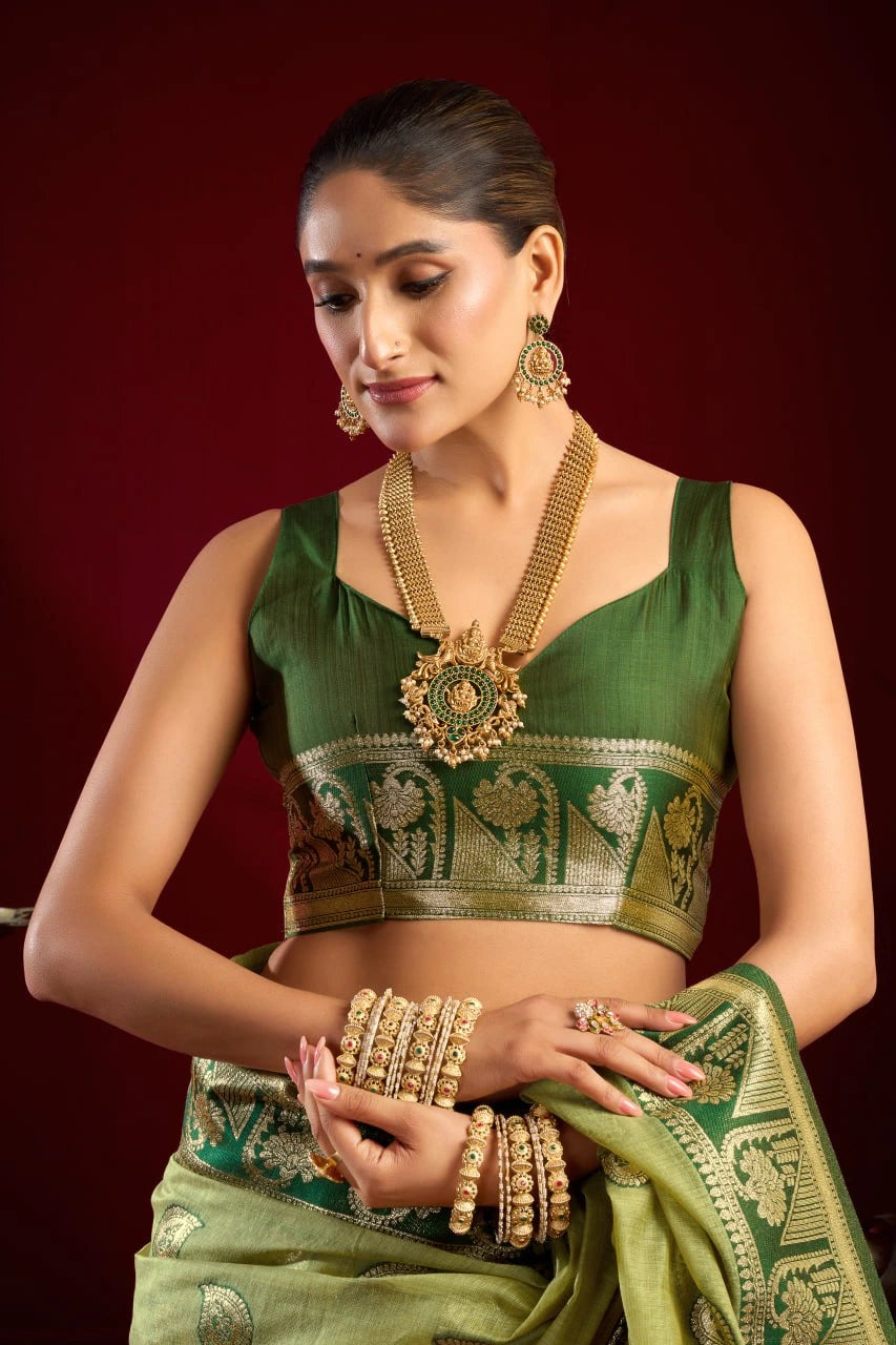 Woman in a green traditional outfit with gold jewelry against a red background