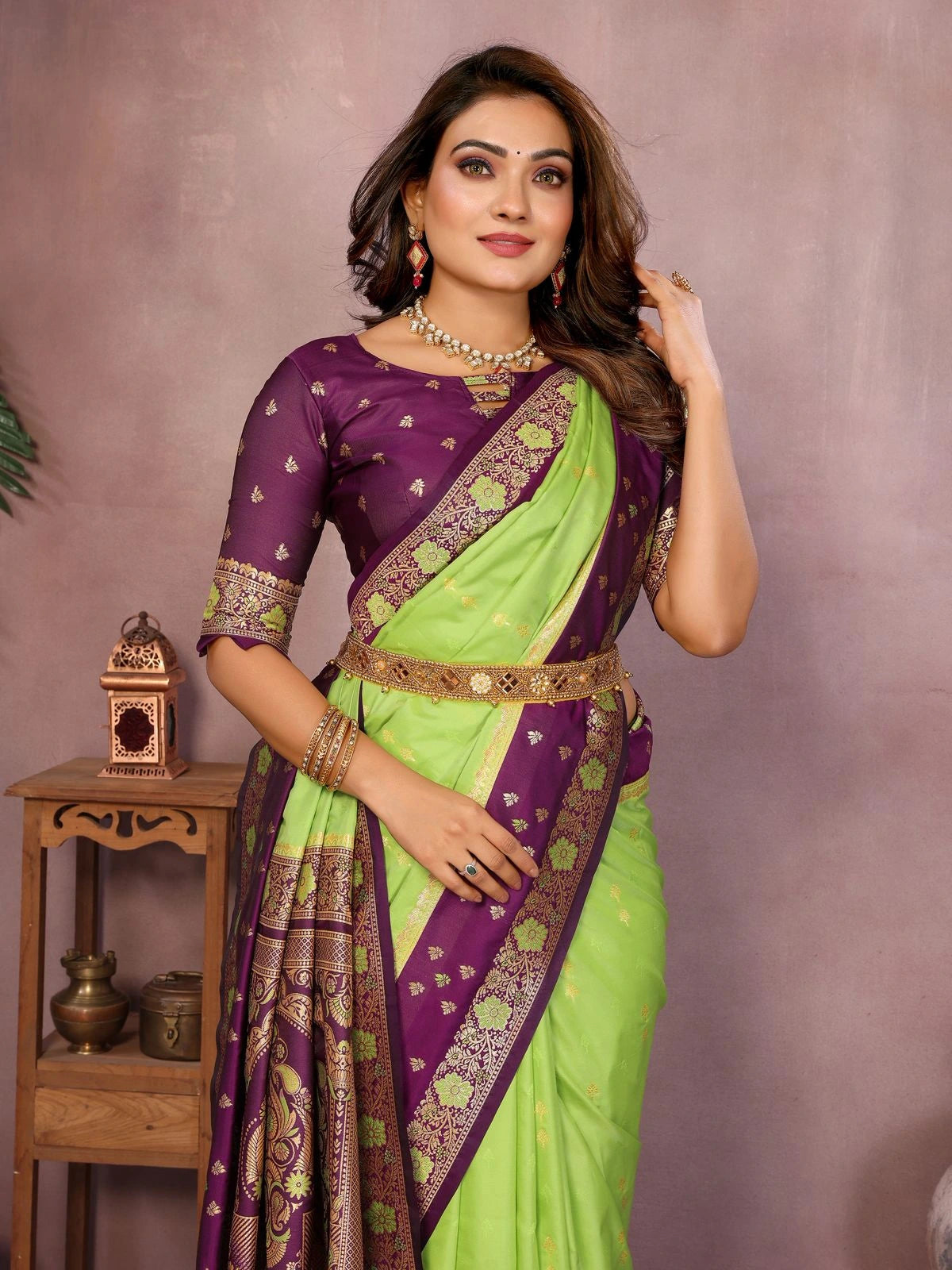 Woman wearing a green and purple saree with jewelry against a neutral background
