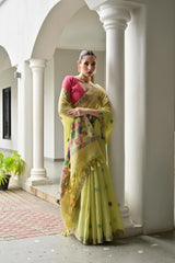 Woman in a yellow saree with floral patterns standing in an architectural setting.