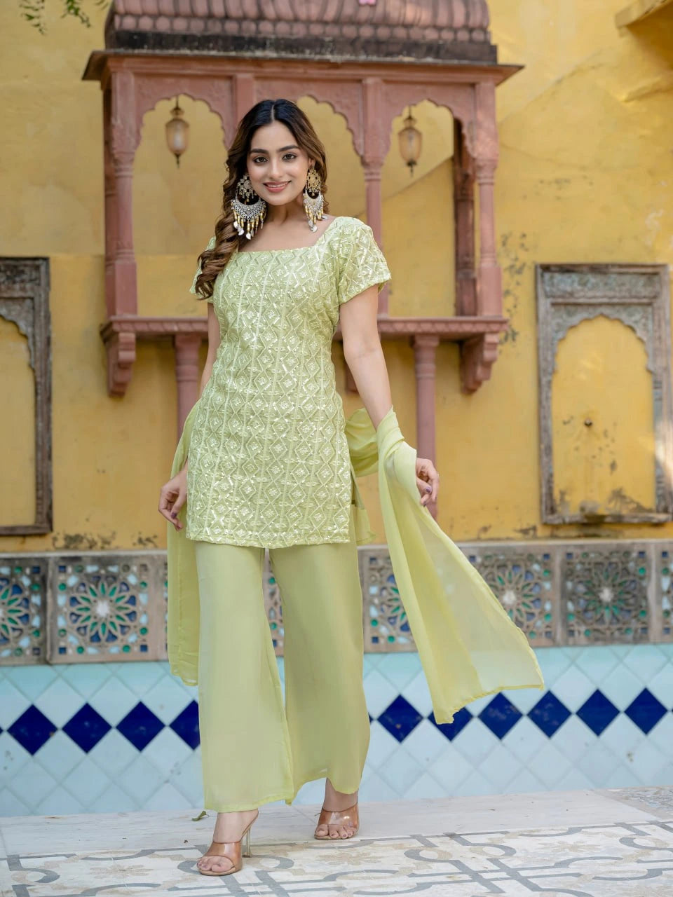 Woman in a light green traditional outfit standing in front of a colorful architectural background