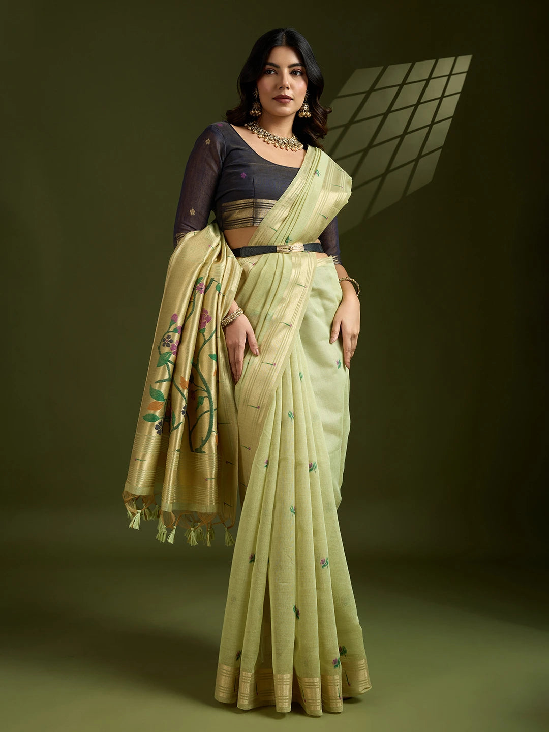 Woman wearing a light green saree with a dark blouse against a dark background