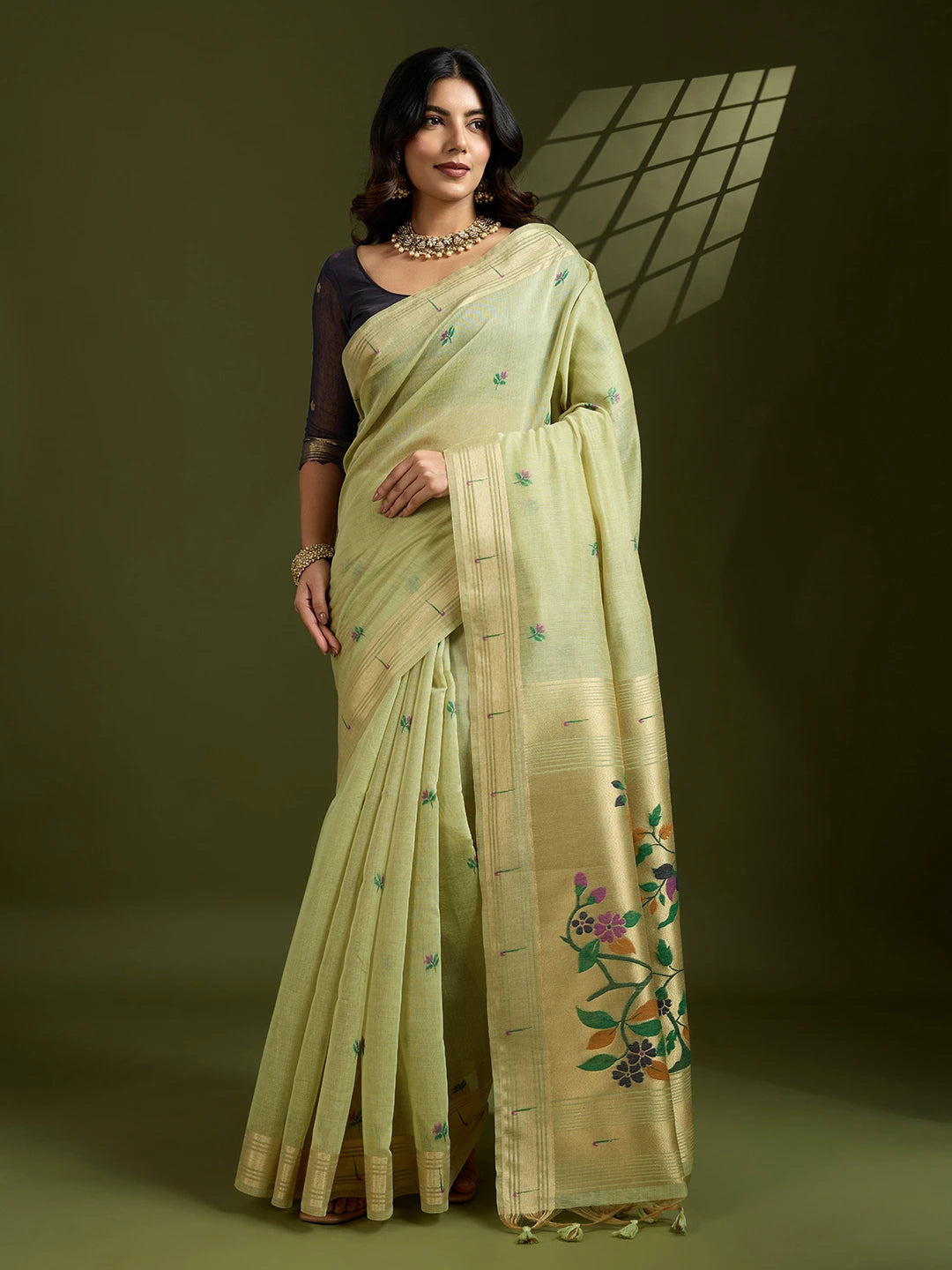 Woman wearing a light green saree with floral patterns on a dark background