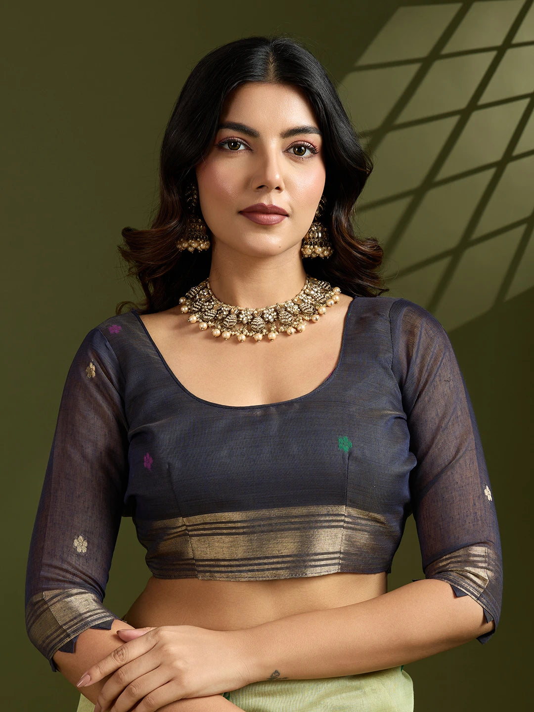 Woman wearing a dark blouse with sheer sleeves against a green background