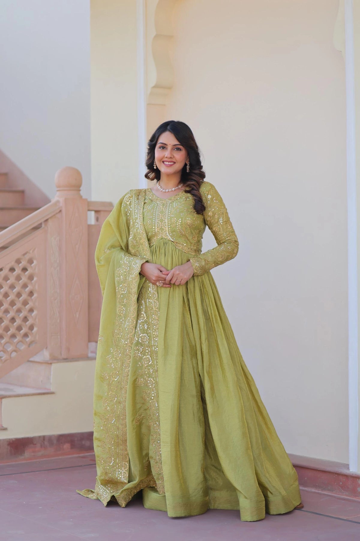 Woman in a green traditional outfit standing indoors with a neutral background