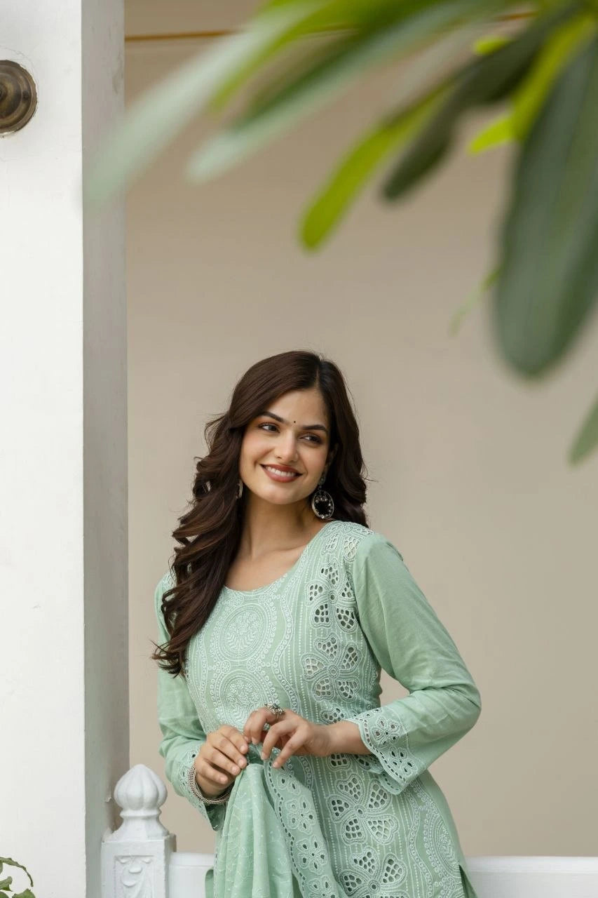 Woman in a light green traditional outfit standing indoors with a neutral background
