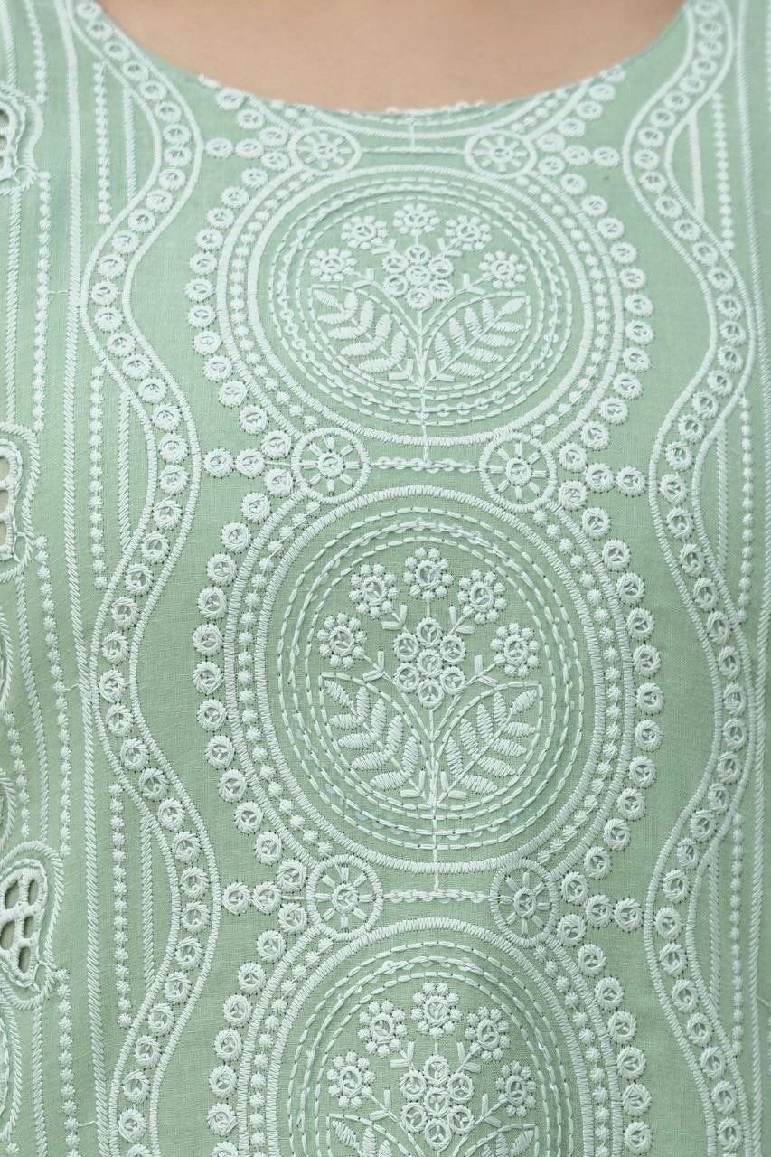 Close-up of a green fabric with intricate white embroidery