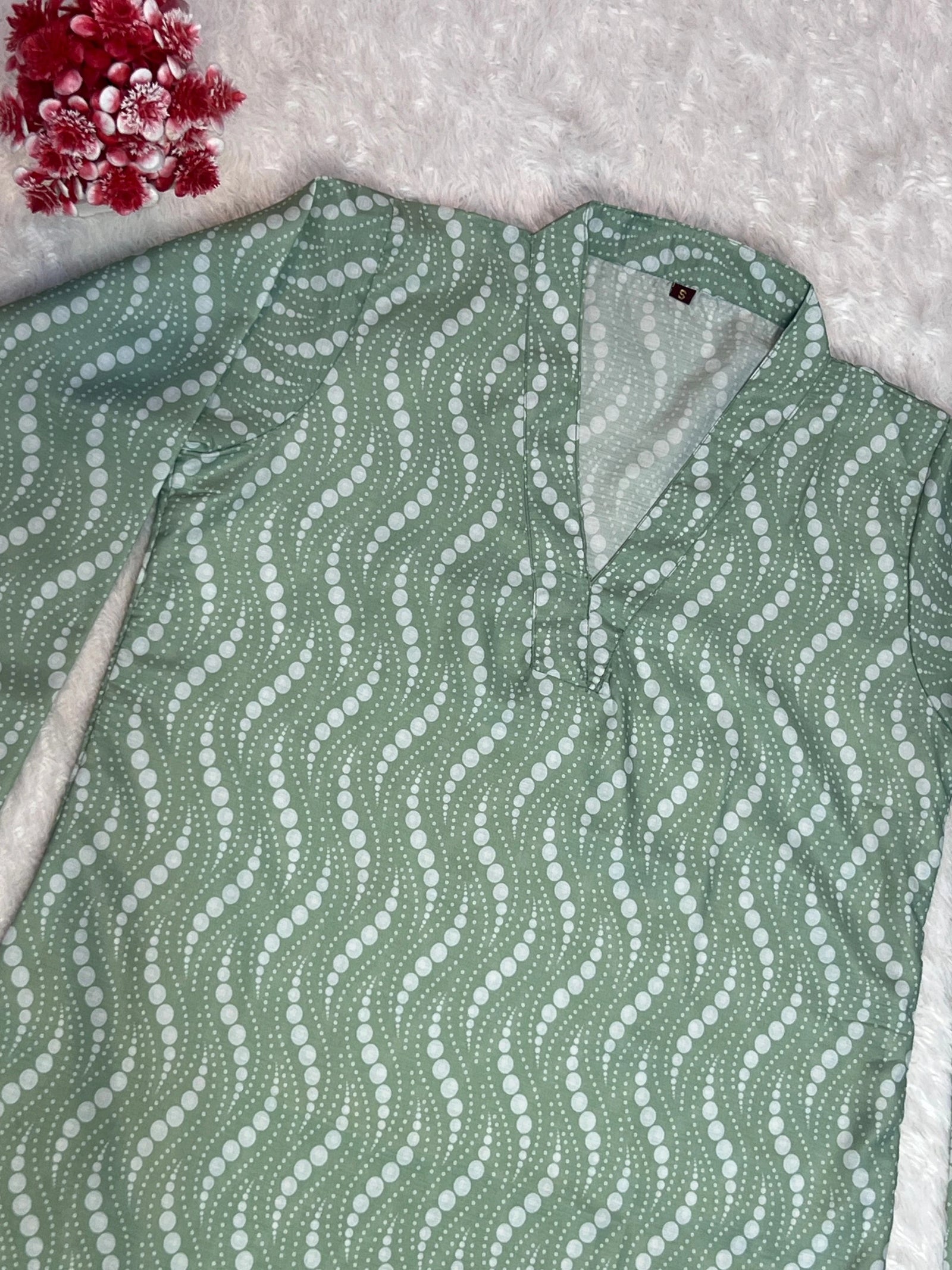 Green patterned shirt on a textured surface with red flowers in the corner