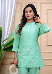 Woman wearing a light green traditional outfit with embroidery, standing indoors.