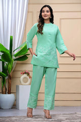 Woman wearing a light green outfit with a plant and decorative items in the background