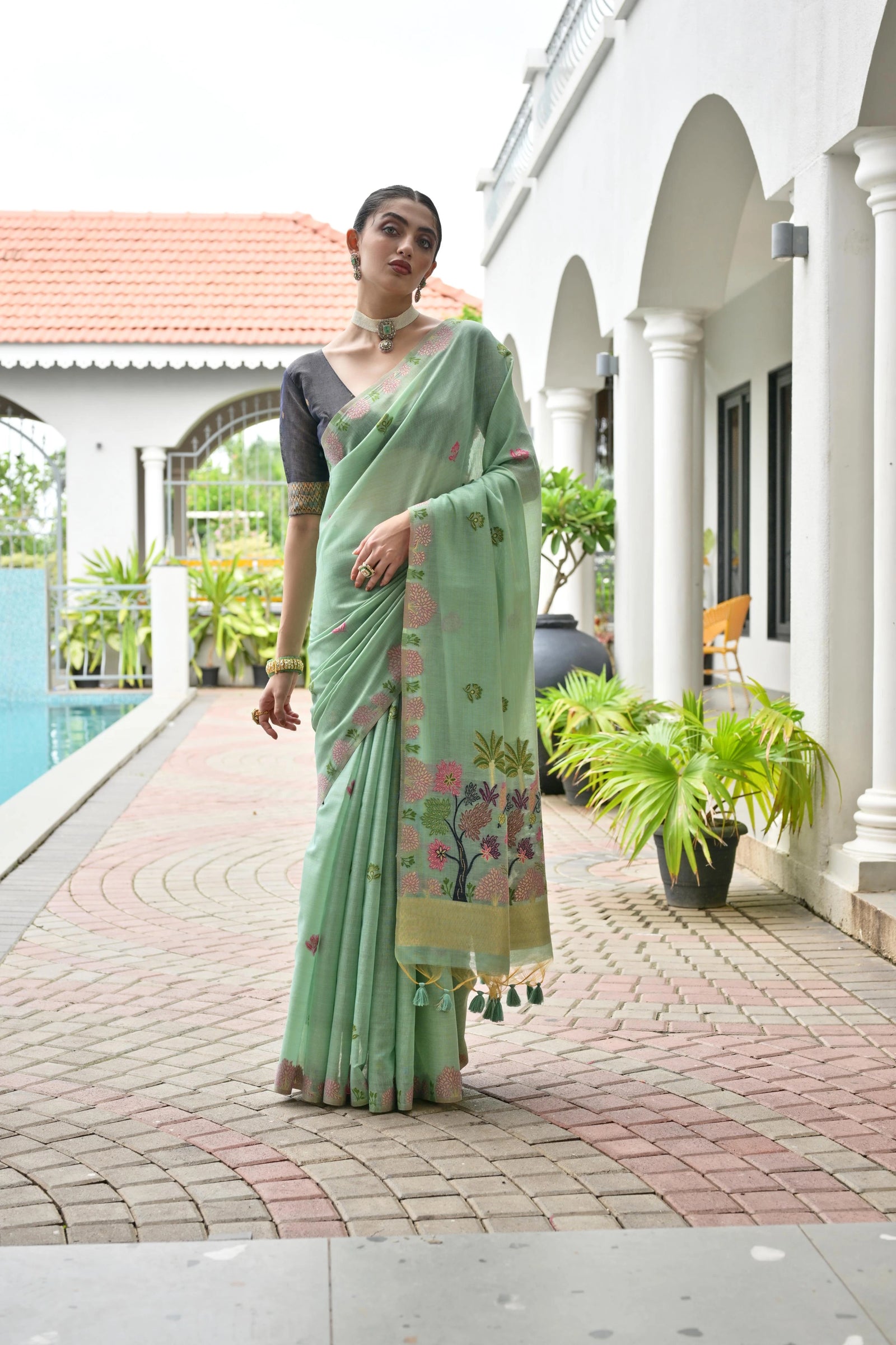 Woman in a light green saree with floral patterns standing on a patio.
