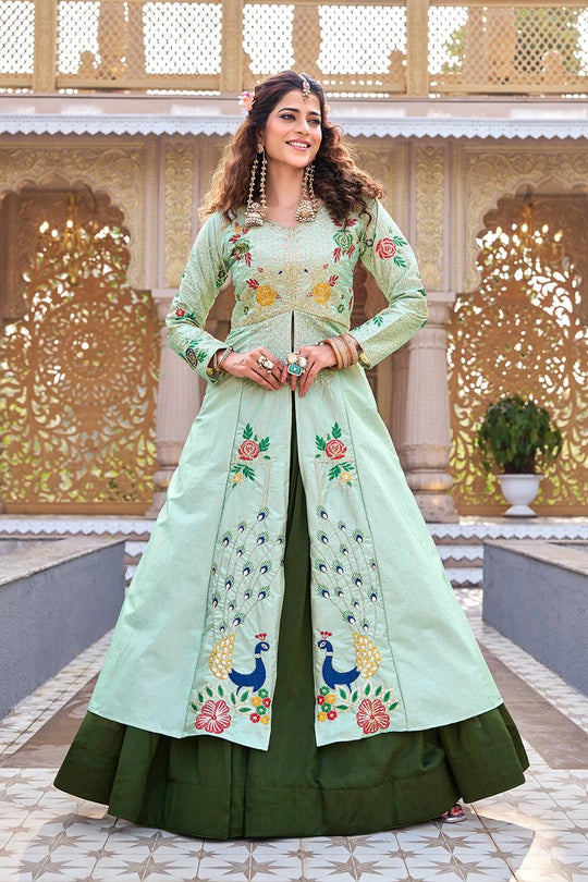 Woman wearing a light green and dark green embroidered traditional outfit in front of an ornate architectural background.