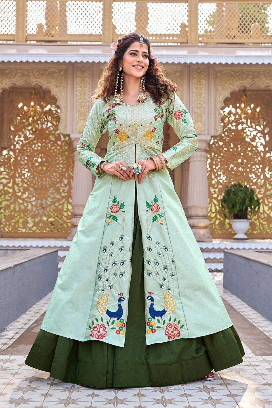 Woman wearing a light green and dark green embroidered traditional outfit in front of an ornate architectural background.