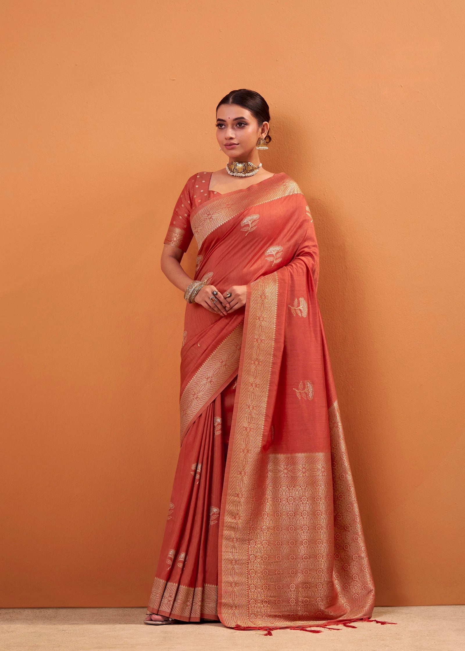 Woman wearing a red saree with gold border against an orange background