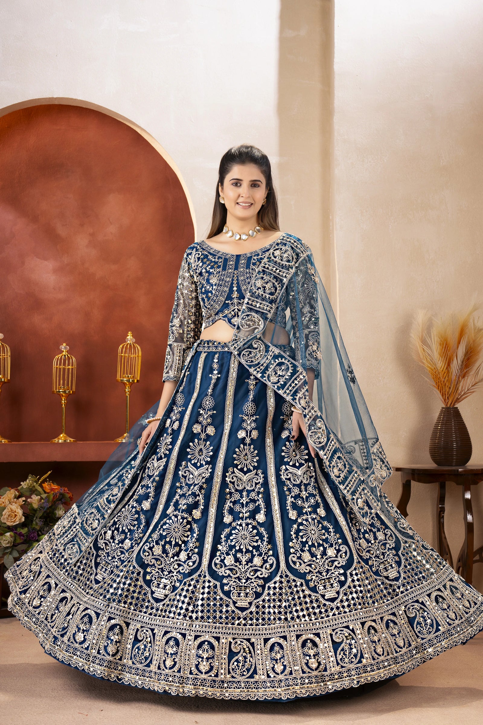 Woman wearing a blue and silver embroidered traditional outfit in a decorated room.