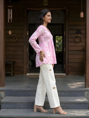 A full-length side-profile shot of a woman smiling and walking across stone steps in front of a wooden house entrance.