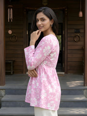A side-profile medium shot of a woman wearing a pink floral tunic, looking toward the camera with her hand on her chin.