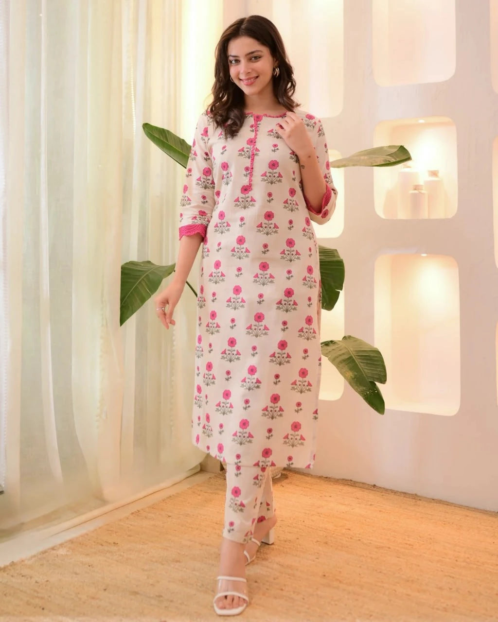 Woman wearing a floral dress in a bright room with plants and lights.
