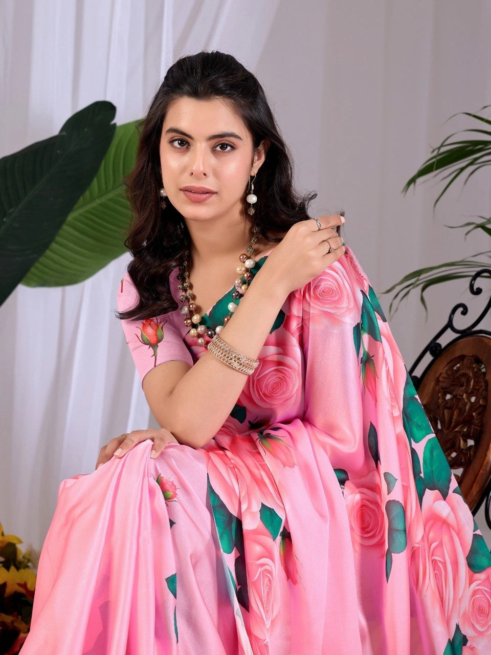 Woman wearing a pink saree with floral patterns against a white curtain background