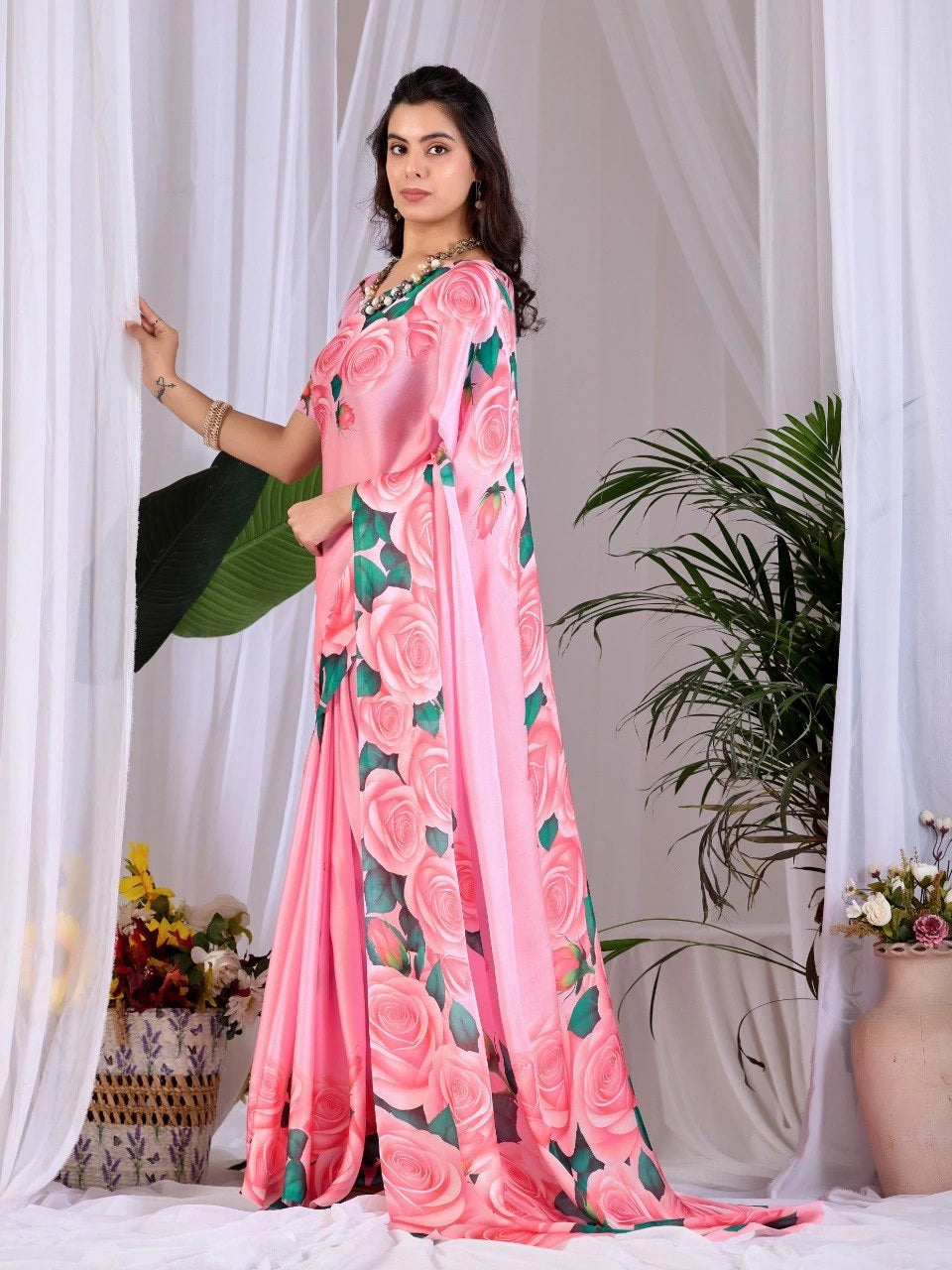 Woman wearing a pink saree with floral patterns against a white curtain background