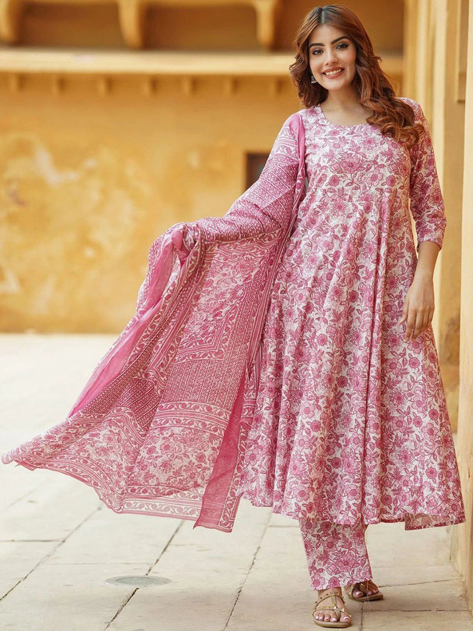 Woman wearing a pink floral outfit standing in front of a beige wall.