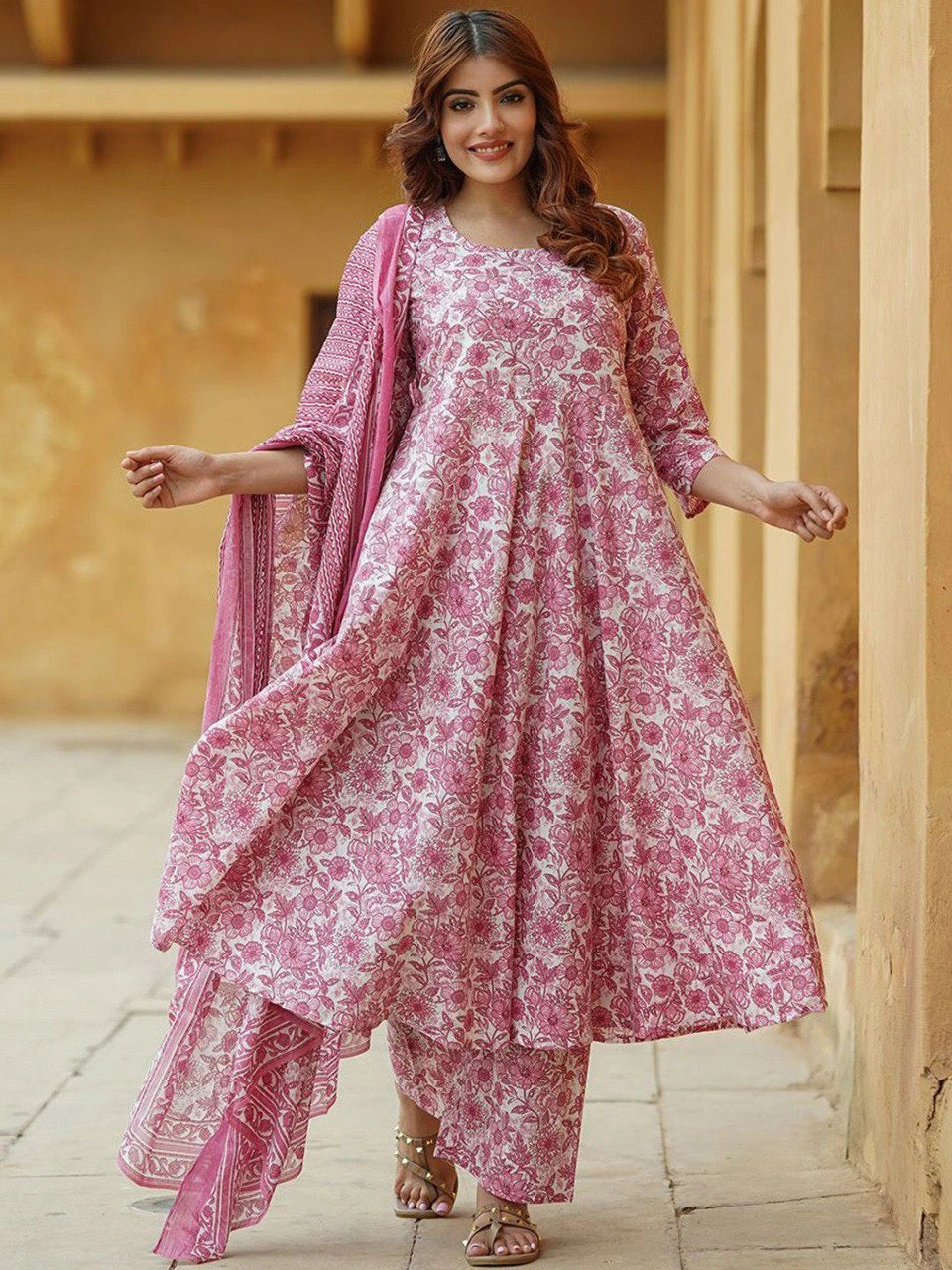 Woman wearing a pink floral traditional outfit with a matching dupatta in an outdoor setting.