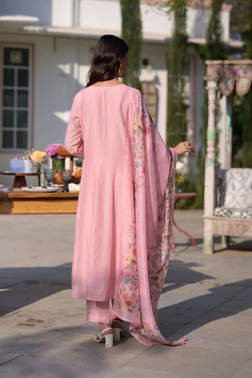 Woman in a pink traditional outfit standing outdoors with a building and garden in the background