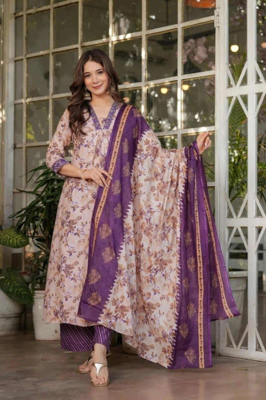 Woman wearing a floral and purple traditional outfit indoors with plants and decor.