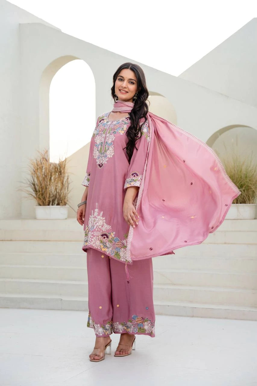 Woman in a pink traditional outfit with floral patterns standing in a white interior setting.