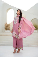 Woman in a pink traditional outfit with floral patterns standing in a white interior setting.