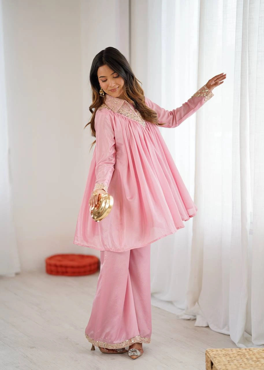 Woman wearing a pink traditional outfit with gold accents in a bright room.