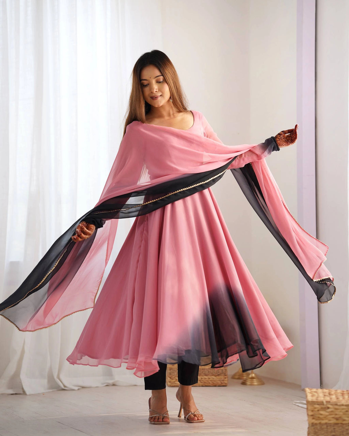 Woman wearing a pink dress with a black border, standing against a white curtain.