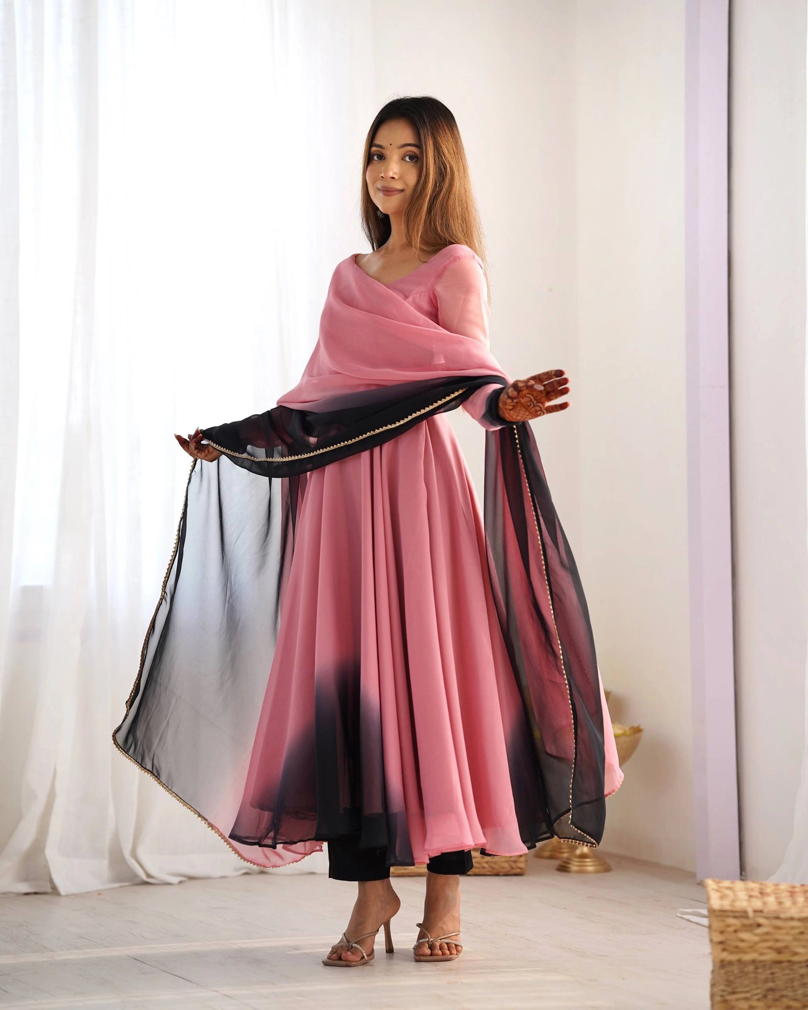 full-length shot of a woman holding her pink and black ombre dupatta wide with both hands, showcasing the flow of her traditional suit.