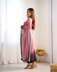 A profile shot of a woman standing in a long pink Anarkali dress with a black ombre hem, looking back over her shoulder towards the camera.