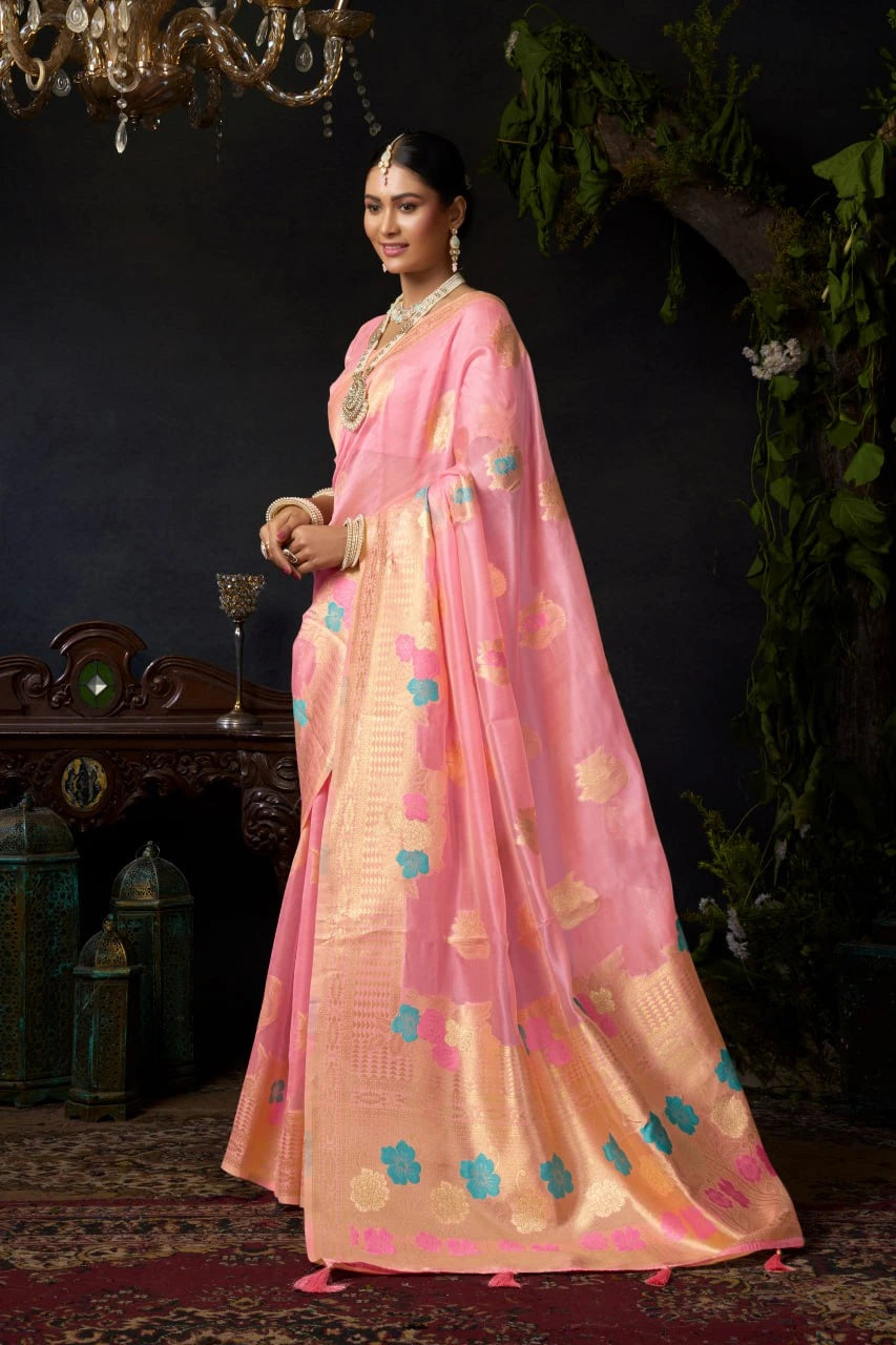 Woman in a pink saree with floral patterns standing in a decorated room.