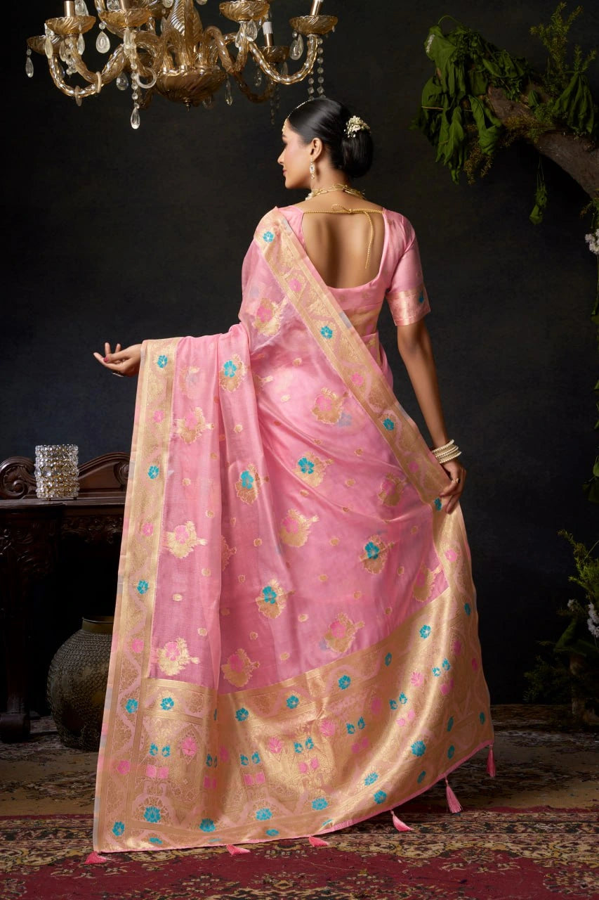 Woman in a pink saree with a gold border standing in a dimly lit room.