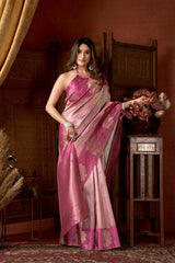 Woman in a pink saree standing in a room with a wooden chair and decorative elements.