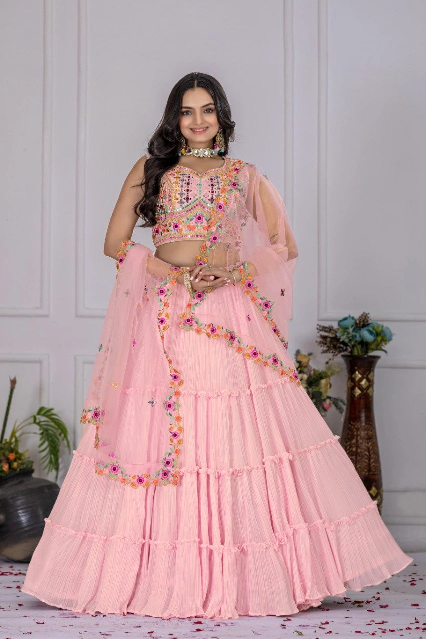 Woman wearing a pink traditional outfit with floral embellishments in a room setting.