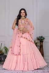 Woman wearing a pink traditional outfit with floral embellishments in a room setting.