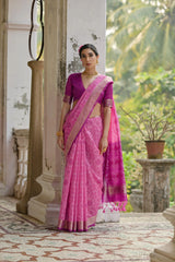 Woman in a pink saree standing outdoors with greenery in the background