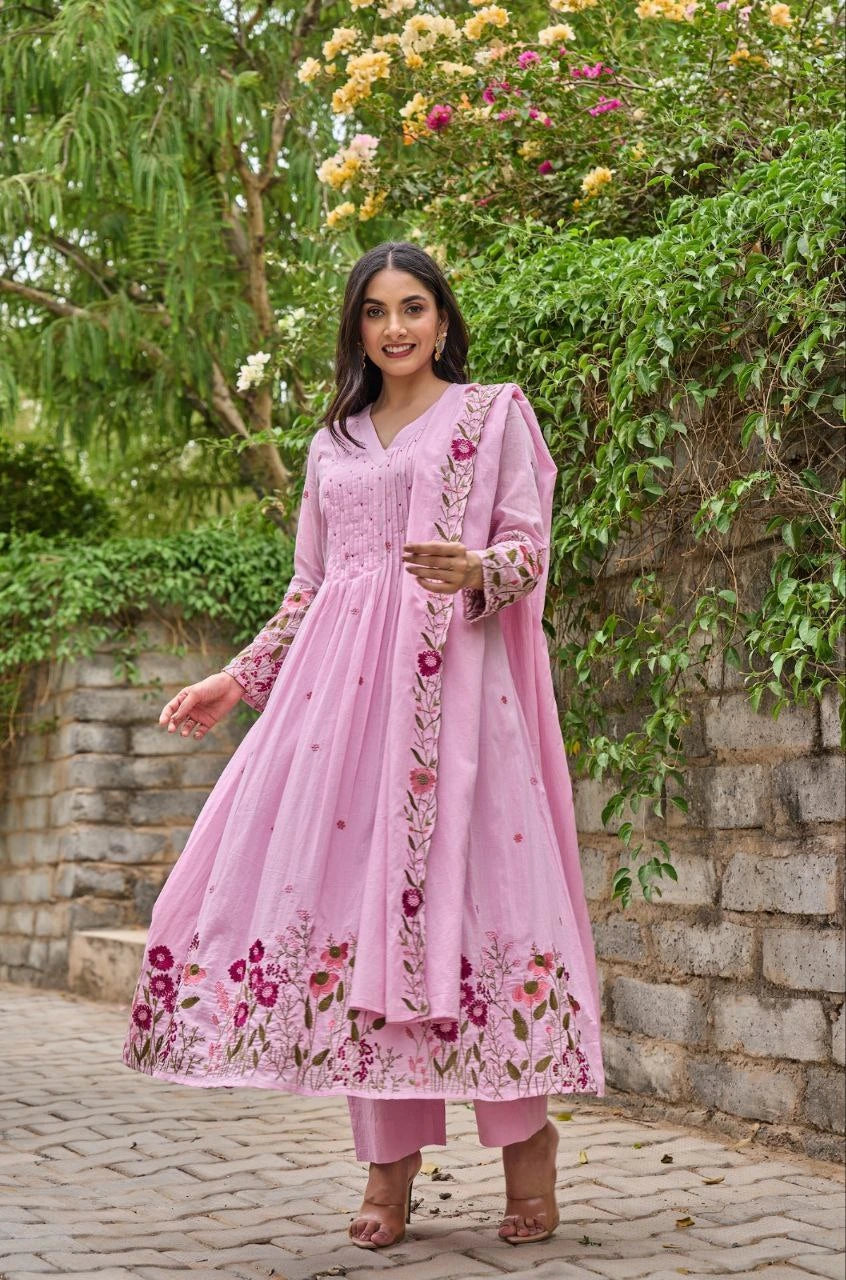 Woman in a pink embroidered outfit standing outdoors with greenery in the background
