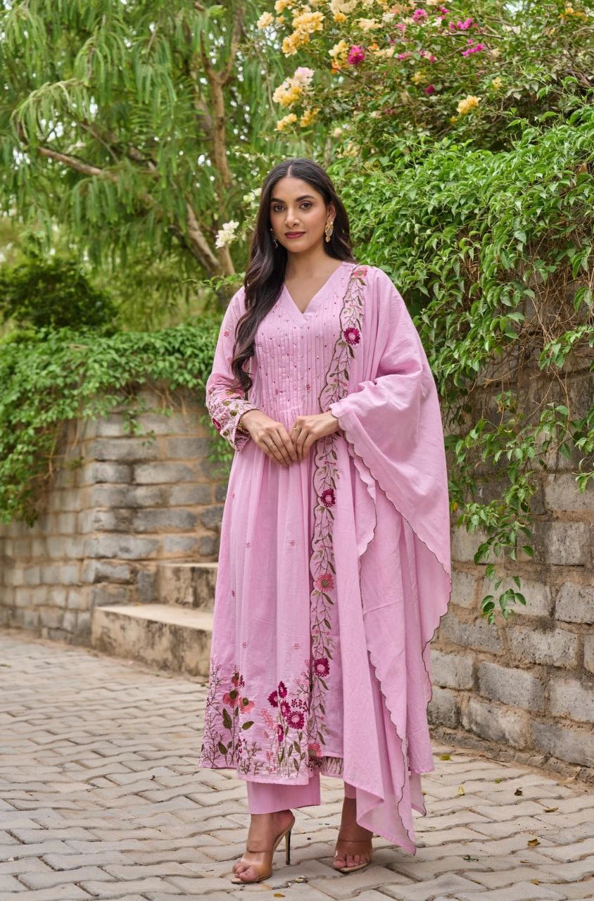 Woman in a pink traditional outfit with floral patterns standing outdoors.