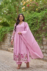 Woman in a pink traditional outfit standing outdoors with greenery in the background