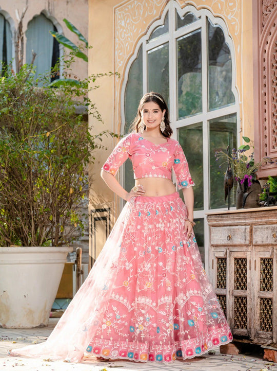 Woman in a pink traditional outfit standing outdoors with decorative elements.