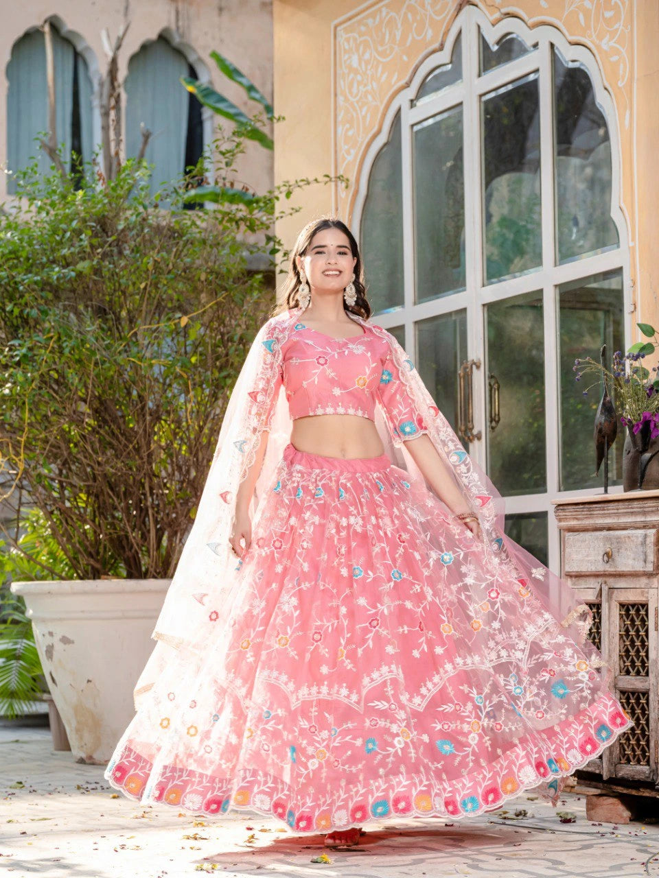 Woman in a pink traditional outfit standing in front of a decorative building entrance.