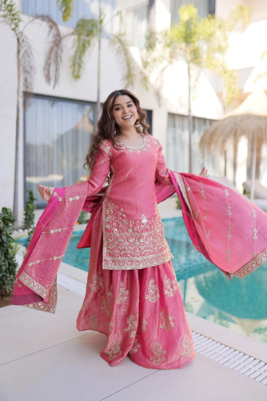 Woman in a pink traditional outfit with gold embroidery standing in front of a modern building.